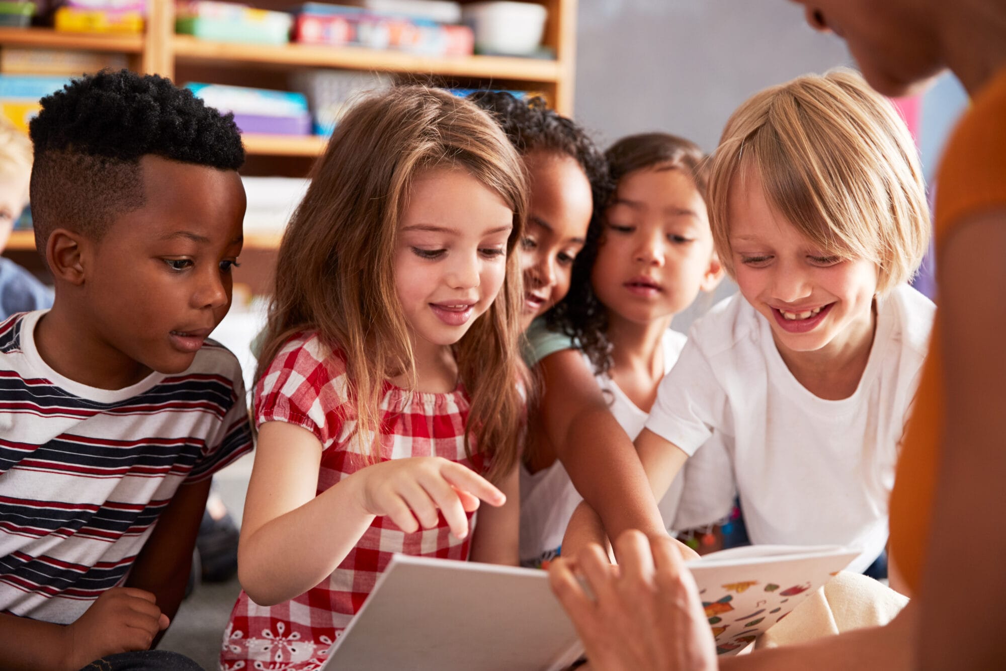 Group Of Elementary School Pupils Sitting On Floor Listening To Female Teacher Read Story